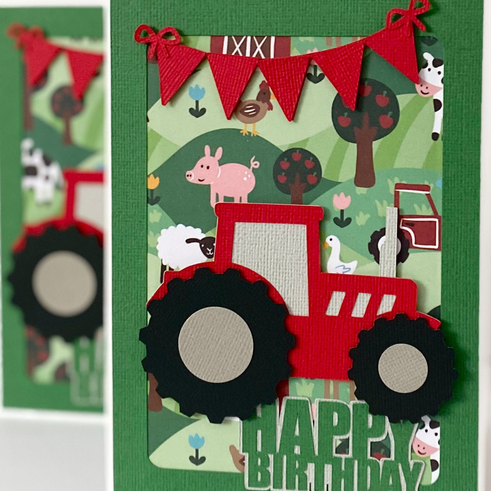 A handmade layered paper card featuring a red tractor with black wheels, a green background with farm animals, and a red bunting banner, with 'HAPPY BIRTHDAY' text at the bottom.